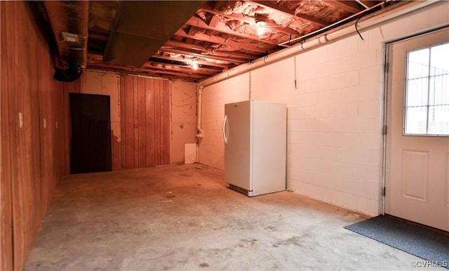 below grade area featuring freestanding refrigerator and concrete block wall