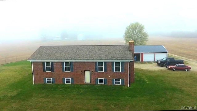 view of front facade with a front yard, a chimney, an outbuilding, brick siding, and a garage