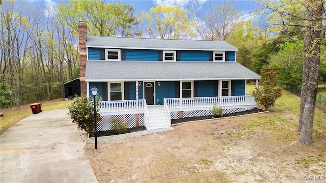 view of front of home featuring a chimney, roof with shingles, concrete driveway, and covered porch