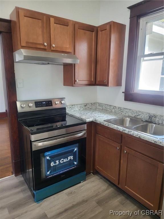 kitchen with electric range, under cabinet range hood, a sink, and light wood-type flooring