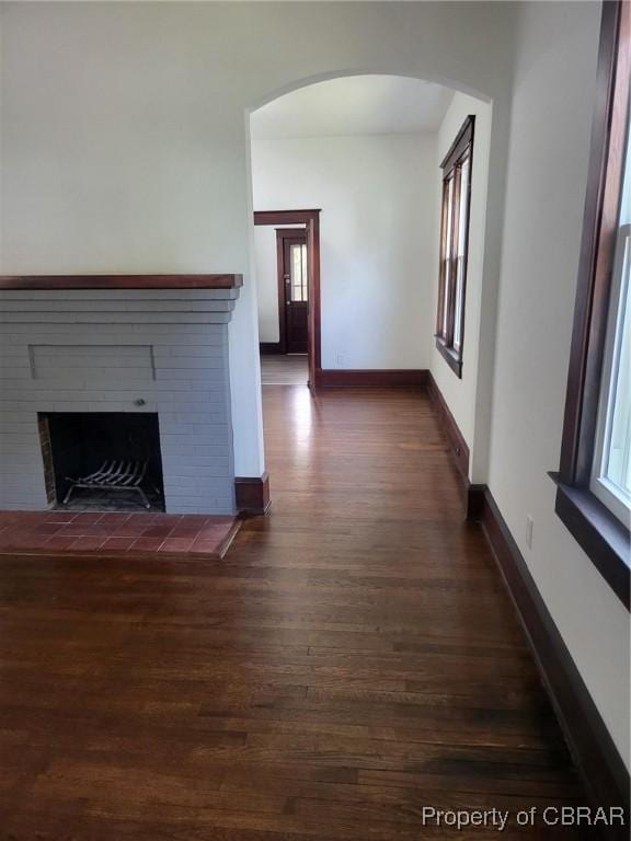 unfurnished living room with arched walkways, dark wood-style flooring, a fireplace, and baseboards