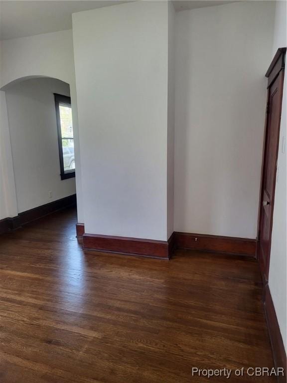 spare room with arched walkways, baseboards, and dark wood finished floors