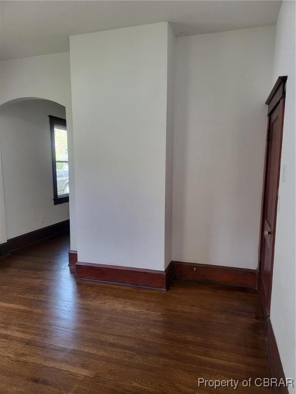 unfurnished room with arched walkways, dark wood-style floors, and baseboards