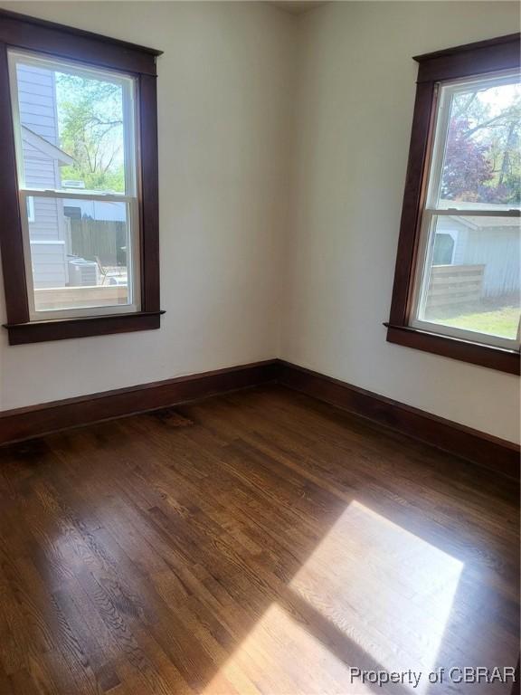empty room featuring a wealth of natural light, baseboards, and dark wood finished floors