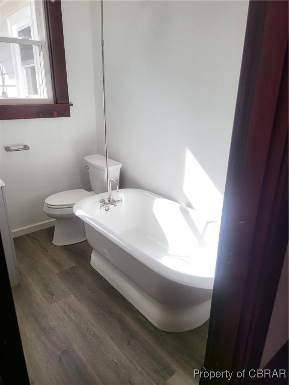 bathroom featuring toilet, a soaking tub, and wood finished floors