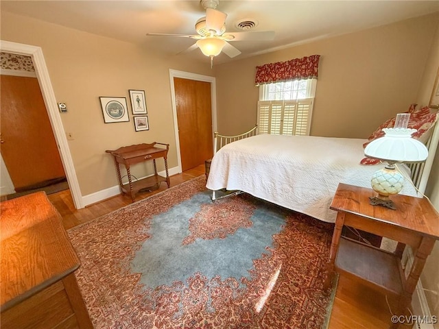 bedroom with ceiling fan, visible vents, baseboards, and wood finished floors
