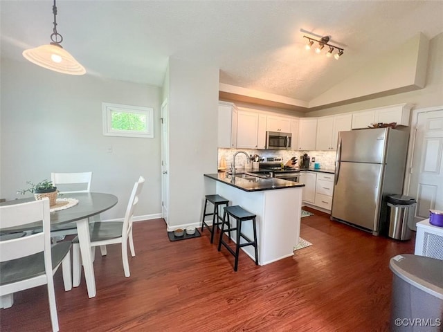 kitchen with a sink, a peninsula, dark countertops, appliances with stainless steel finishes, and lofted ceiling
