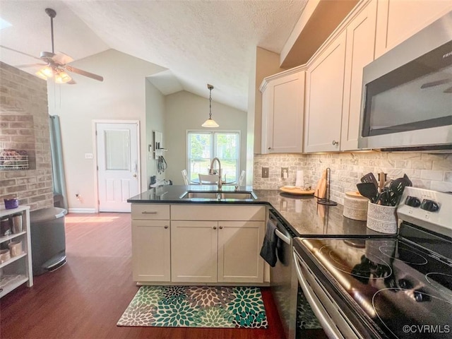 kitchen featuring stainless steel appliances, vaulted ceiling, dark countertops, a sink, and a peninsula
