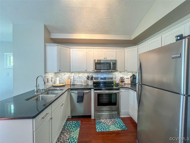 kitchen with appliances with stainless steel finishes, a sink, white cabinetry, a peninsula, and dark wood-type flooring