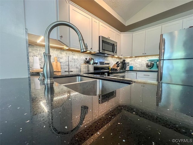 kitchen with dark stone countertops, white cabinets, stainless steel appliances, and backsplash