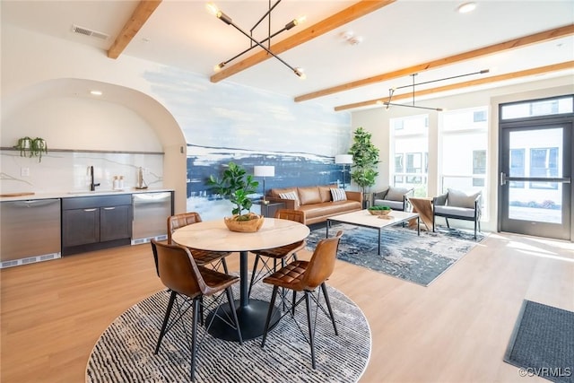 dining space featuring visible vents, light wood-style flooring, a community bar, and beamed ceiling
