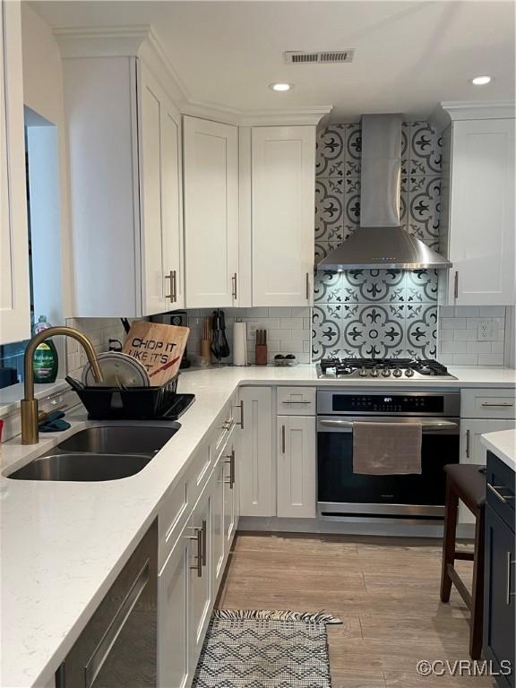 8304 Elizabeth Ann Dr, Hanover, VA 23111 - kitchen featuring appliances with stainless steel finishes, wall chimney exhaust hood, a sink, white cabinetry, and light wood-type flooring