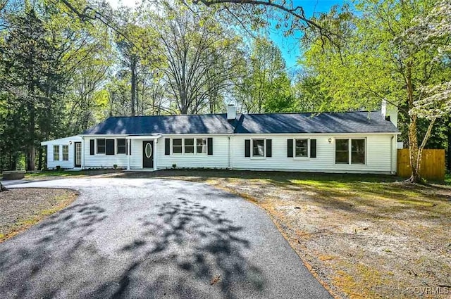 ranch-style home featuring driveway, a chimney, and fence
