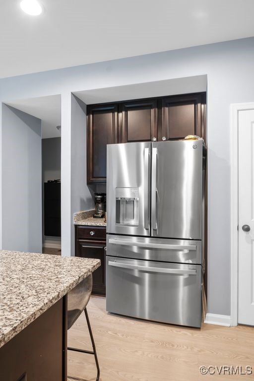 kitchen featuring dark brown cabinetry, stainless steel fridge with ice dispenser, baseboards, light stone counters, and light wood finished floors