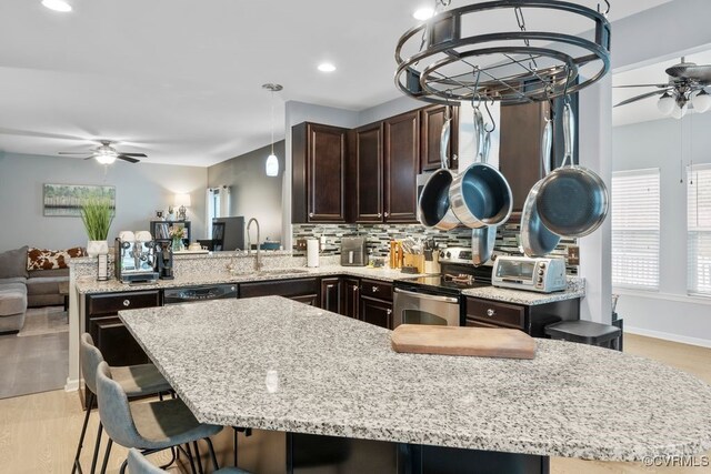 kitchen with a ceiling fan, electric range, dark brown cabinets, light stone counters, and a sink