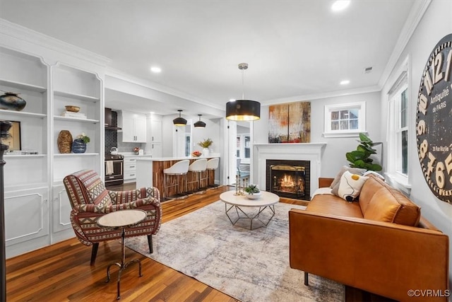 living room featuring a warm lit fireplace, crown molding, wood finished floors, and recessed lighting
