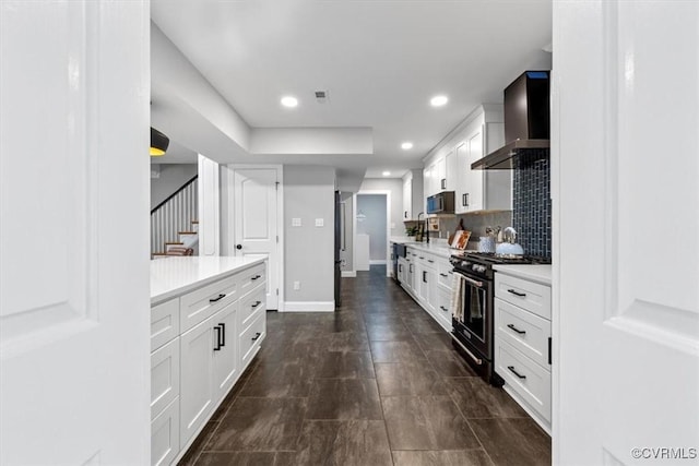 kitchen featuring black microwave, light countertops, white cabinets, wall chimney exhaust hood, and gas stove