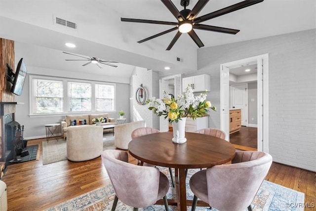 dining space featuring brick wall, ceiling fan, wood finished floors, and visible vents