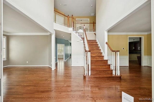 stairway with wood finished floors, a decorative wall, a high ceiling, and a wainscoted wall