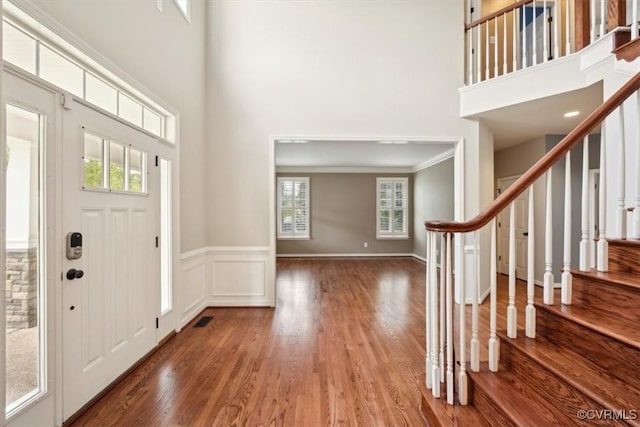 foyer featuring a high ceiling, wainscoting, stairs, wood finished floors, and visible vents