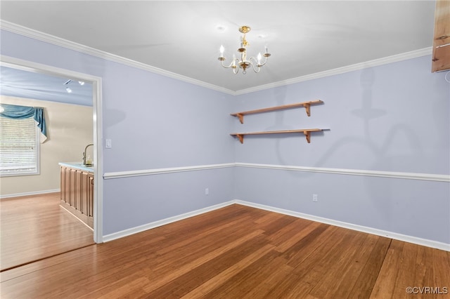 spare room with wood finished floors, an inviting chandelier, baseboards, and ornamental molding
