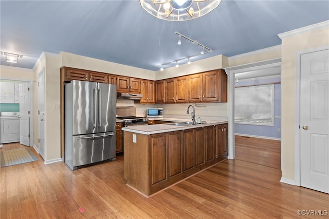 kitchen with a sink, a peninsula, under cabinet range hood, independent washer and dryer, and stainless steel appliances