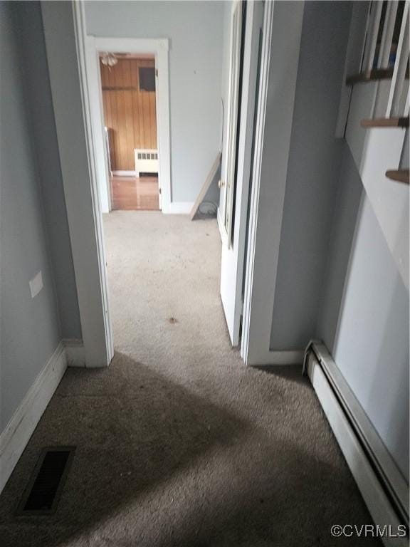 hall with a baseboard heating unit, baseboards, visible vents, radiator, and carpet