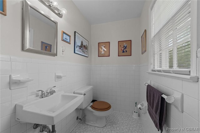 bathroom with tile patterned flooring, toilet, wainscoting, tile walls, and a sink