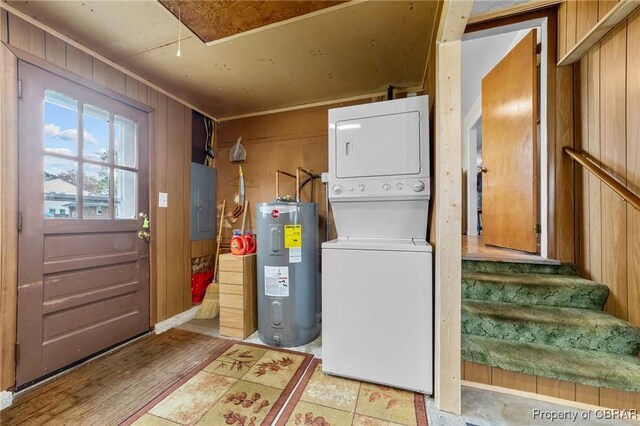 laundry area featuring electric water heater, electric panel, wooden walls, and stacked washer and dryer