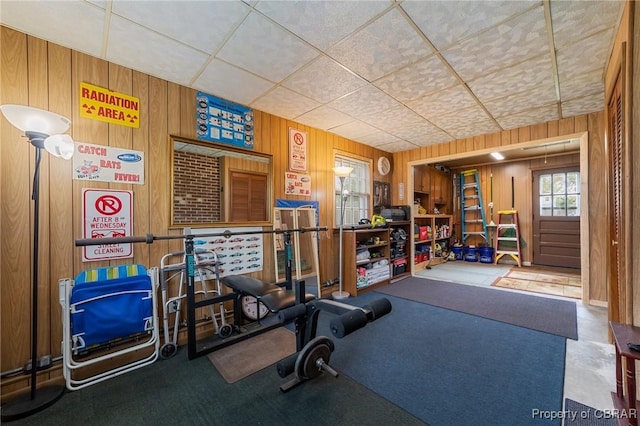 exercise room featuring wooden walls and a drop ceiling