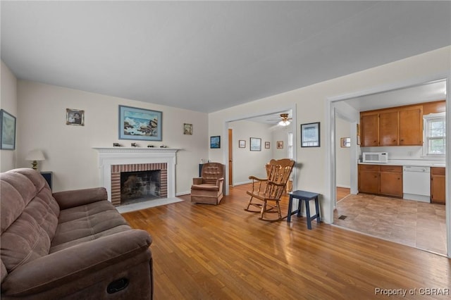 living room featuring light wood-style floors, a fireplace, and a ceiling fan
