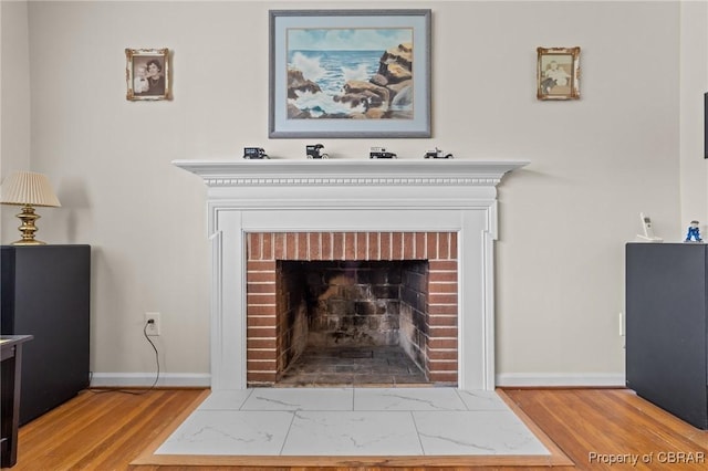 room details featuring a brick fireplace, baseboards, and wood finished floors