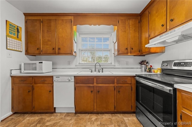 kitchen with white appliances, light countertops, under cabinet range hood, brown cabinetry, and a sink