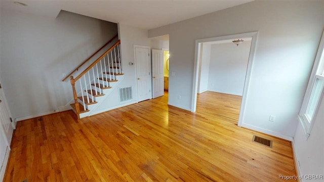 unfurnished living room with light wood-style floors, visible vents, and stairs