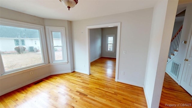 empty room featuring visible vents, light wood-style flooring, stairway, and baseboards