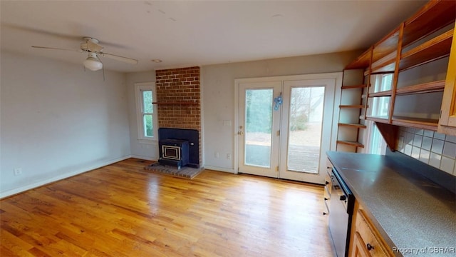 unfurnished living room featuring a wood stove, light wood-style floors, baseboards, and a ceiling fan