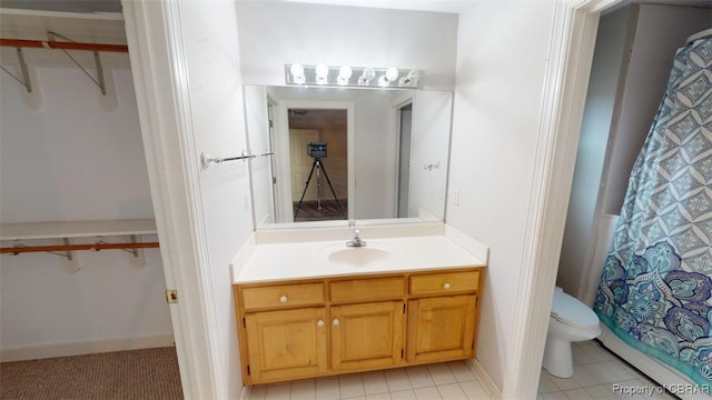 bathroom featuring tile patterned flooring, vanity, a walk in closet, and toilet