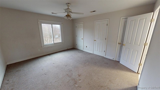 unfurnished bedroom featuring visible vents, baseboards, ceiling fan, carpet, and multiple closets