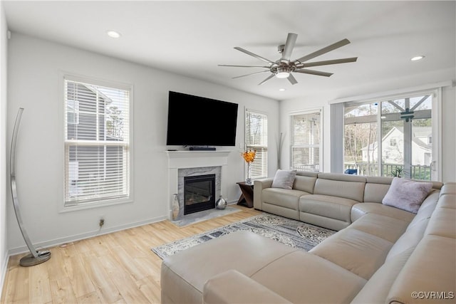 living area featuring ceiling fan, light wood-type flooring, a fireplace, and a healthy amount of sunlight