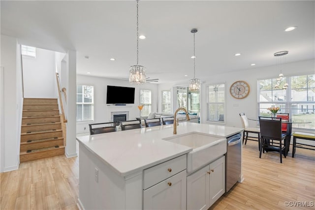 kitchen featuring light wood-style flooring, stainless steel dishwasher, a sink, and a fireplace