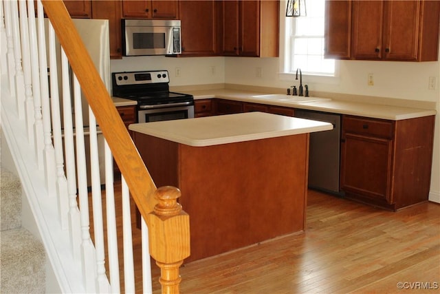 kitchen with a sink, stainless steel appliances, light wood finished floors, light countertops, and a center island