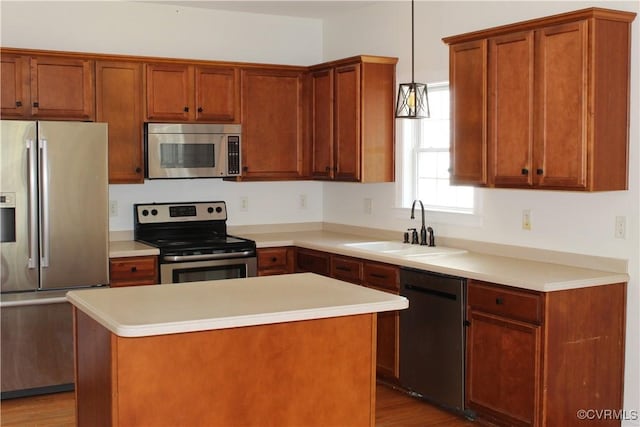 kitchen with stainless steel appliances, hanging light fixtures, a sink, a kitchen island, and light countertops