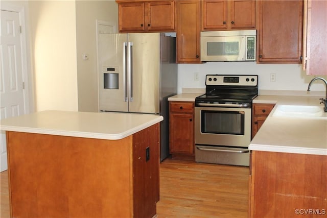 kitchen featuring a sink, brown cabinetry, light wood finished floors, a kitchen island, and appliances with stainless steel finishes