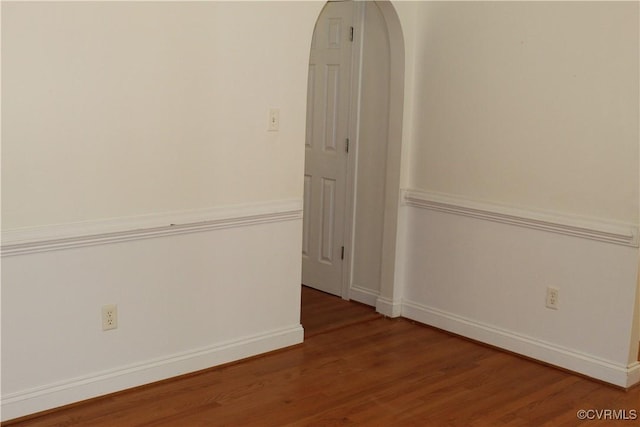 spare room with arched walkways, baseboards, and wood finished floors