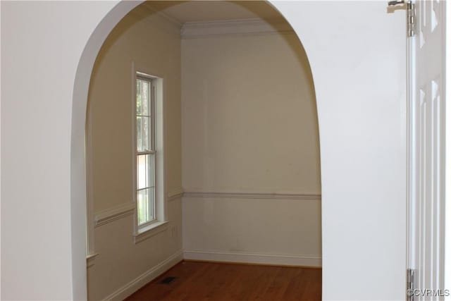 spare room featuring wood finished floors, crown molding, visible vents, baseboards, and arched walkways