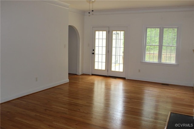 empty room with crown molding, arched walkways, baseboards, and wood finished floors