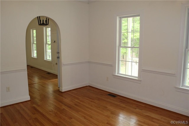 empty room featuring baseboards, arched walkways, light wood-type flooring, and visible vents