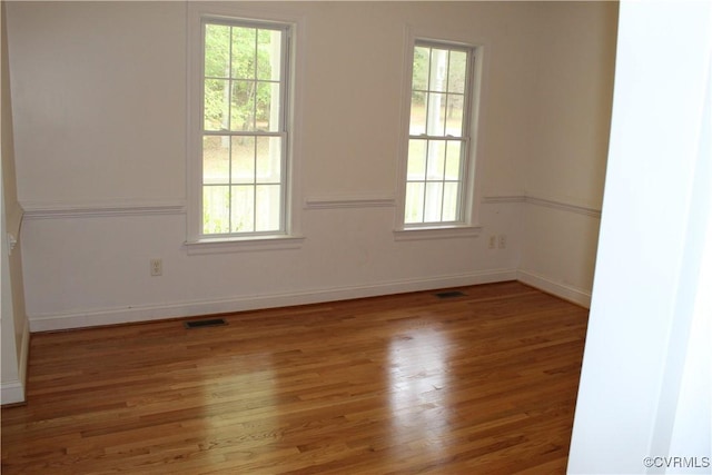 empty room featuring baseboards, visible vents, and wood finished floors
