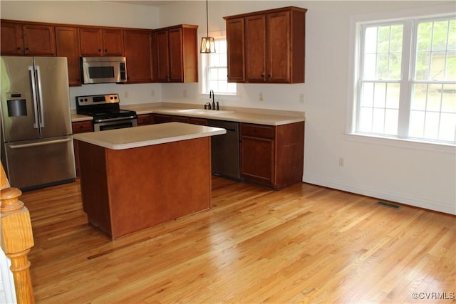 kitchen with a sink, decorative light fixtures, light wood finished floors, a center island, and appliances with stainless steel finishes