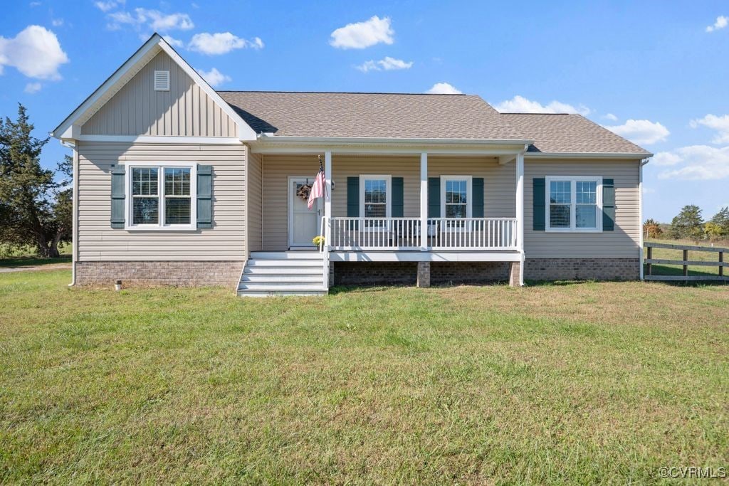 view of front of property with board and batten siding, covered porch, roof with shingles, a front yard, and fence